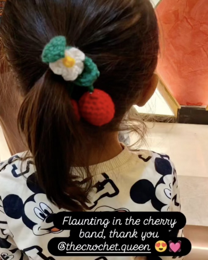 A red crochet cherry hair band with a white flower, worn in a ponytail